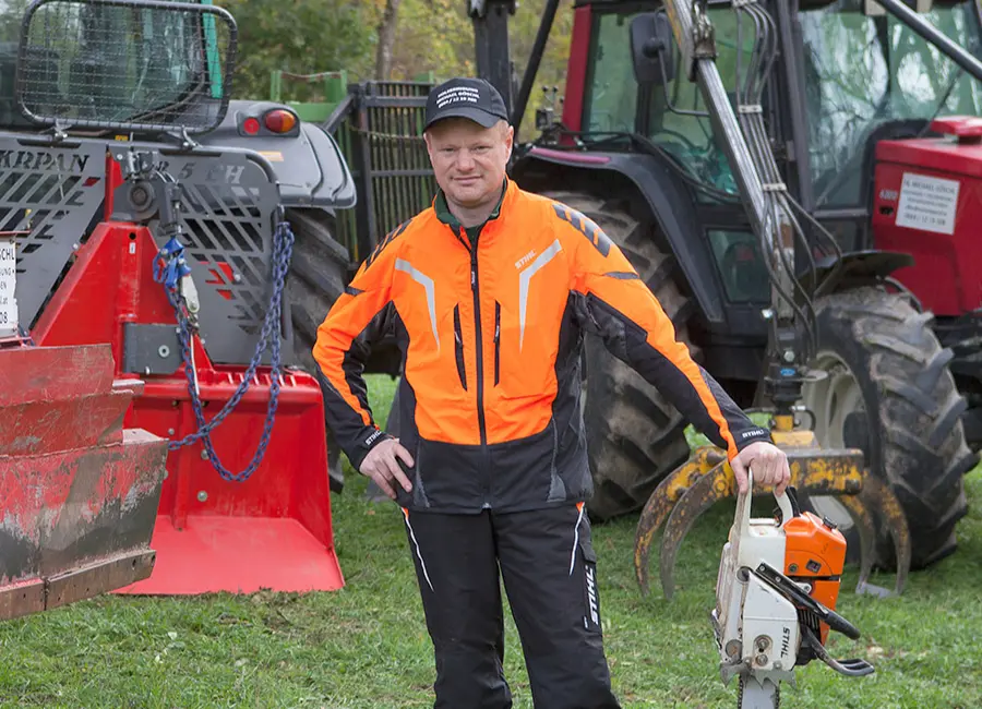 Michael Göschl von Göschlholz vor seinem forstwirtschaftlichen Fuhrpark mit einer Kettensäge.